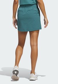 Zielono-czarna mini spódniczka w kratę z dopasowaną talią, bocznymi kieszeniami i linią dołu powyżej połowy uda, w zestawieniu z białymi butami sportowymi.