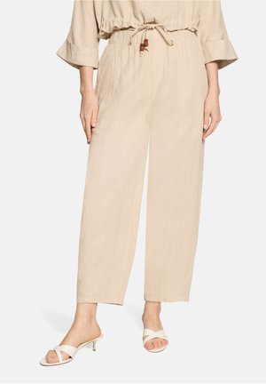 Beige vidde bukser med elastisk talje og snor, stylet med cremefarvede åben tå hælede sandaler på en stående model.