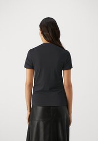 T-shirt noir à manches courtes en tissu doux avec un design classique à col rond. La coupe est ajustée avec une texture lisse.