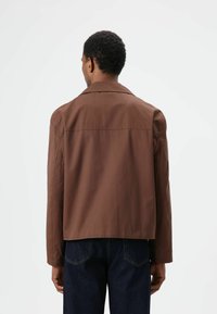 Lichtbruin jack van lightweight materiaal met een kraag, rechte snit en lange mouwen. Gladde textuur, minimale stiksels en een ontspannen ontwerp.