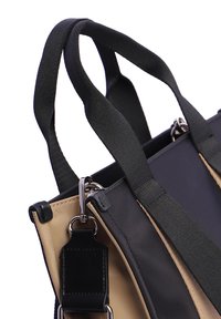 Primer plano de asas de bolso en negro y beige con correa de hombro negra desmontable y herrajes de metal plateado.