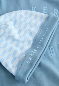 Svetlomodrá pletená čiapka s opakujúcim sa vzorom "BAKER" v svetlejšom odtieni. Má pevný modrý lem s vyšitým nápisom "BAKER by TED BAKER".