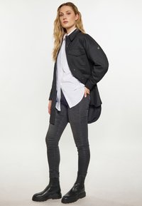 Czarna, oversize'owa kurtka z dwiema kieszeniami na piersi, noszona na białej koszuli. Modelka ma na sobie ciemne, obcisłe dżinsy i czarne botki za kostkę.