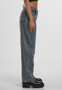 High-waisted, straight-leg jeans in faded blue denim, featuring five pockets and a classic waistband. Worn with chunky black platform boots.