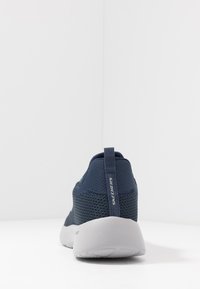 Marineblaue Sportsneaker mit einem strukturierten Mesh-Obermaterial und einer grauen Gummisohle. Verfügt über einen Zugriemen an der Ferse und "SKECHERS"-Markierung an der Seite.