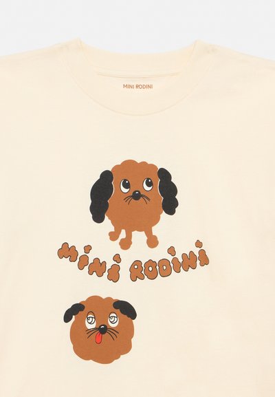 Camisa creme com dois cães de desenho animado castanhos, um com orelhas pretas moles olhando para cima e o outro com a língua de fora; texto "MINI RODINI" entre os cães.