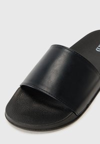 Svart halksandaler med en slät, blank syntetisk ovandel och en texturerad gummisula. Avslappnad design med öppen tå och bred rem.