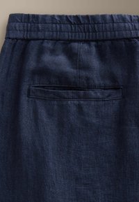 Tissu bleu marine avec une taille élastique et une poche passepoilée horizontale à l'arrière d'un vêtement.