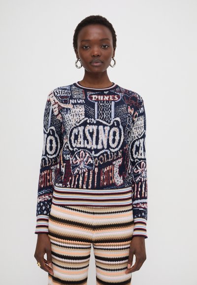 Pull en maille avec un design graphique de casino multicolore, encolure ronde et manches à rayures côtelées. Associé à un pantalon en maille à motifs.