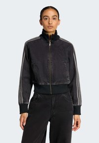 Crna cropped traper jakna s patent zatvaračem sprijeda, rebrastim manžetnama i visokim ovratnikom; s kontrastnim prugama koje se protežu duž rukava.