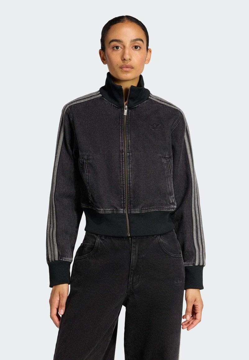 Crna cropped traper jakna s patent zatvaračem sprijeda, rebrastim manžetnama i visokim ovratnikom; s kontrastnim prugama koje se protežu duž rukava.