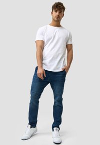 Camiseta blanca de manga corta combinada con jeans azul oscuro de corte recto y detalles sutiles de costura. Completado con zapatillas blancas.