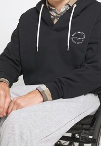 Felpa nera con scollatura a V e coulisse bianche. Include una grafica circolare stampata. Pantaloni grigi con finitura testurizzata.