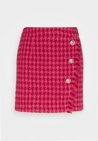 Jupe en tissu rose avec un motif pied-de-poule, quatre boutons décoratifs dorés sur un côté, et un ourlet effiloché.
