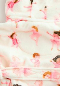 Mjuk vit fleecebadrock med rosa dansare i olika frisyrer, mot en ljus rosa och röd prickig bakgrund.