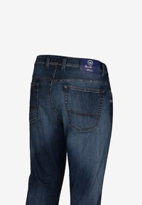 I jeans in denim blu scuro presentano un design a gamba dritta, due tasche posteriori e un'etichetta con marchio sulla vita con dettagli di cuciture a contrasto.