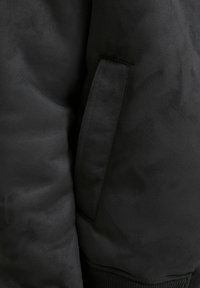 Crna bomber jakna s mekanim, teksturiranim materijalom, bočnim džepom i rebrastim manžetama. Dizajn je elegantan s minimalnim detaljima šavova.