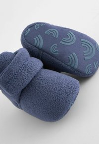 Pehmeät siniset fleece-sandaalit, joissa on teksturoitu, kumimainen pohja, jossa on vaaleansinisten puolikuun muotoisten geometrinen kuvio.