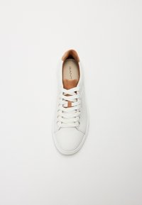White leather sneaker with a tan suede accent on the tongue and gold eyelets, featuring white laces and a smooth texture.