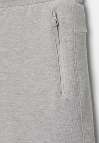 Jogger en tissu texturé gris avec une poche zippée sur le côté et une glissière lisse. Design doux et décontracté adapté pour les vêtements de sport.
