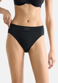 Schwarze Baumwollslips mit glatter Textur, einem breiten elastischen Bund und minimalistischem Design, das dezente Markenkennzeichnung am Bund aufweist.