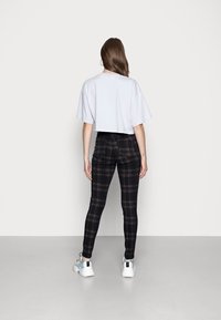 Camiseta corta de color azul claro combinada con pantalones de cuadros negros de cintura alta, mostrando una mezcla de azules, marrones y amarillos, llevada con zapatillas blancas.