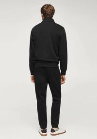 Felpa nera e pantaloni jogger, realizzati in tessuto morbido, con una vestibilità comoda e polsini a costine, abbinati a sneaker bianche.