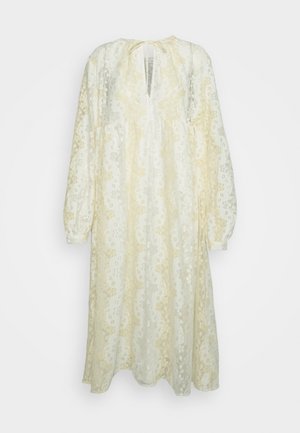 Krajkové šaty krémové barvy s květinovými vzory v odstínech žluté. Dlouhé rukávy, volný střih, výstřih do V a detail sázky na zavazování na zádech.
