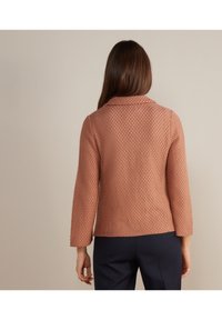 Růžová texturovaná bunda s límcem a rukávy po lokty. Zadní část má jemný geometrický vzor. Mírně přiléhavý střih.