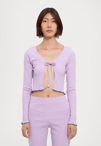 Lilac cropped long-sleeve top with a tie closure at the front, featuring ribbed texture and scalloped edges, paired with matching bottoms.