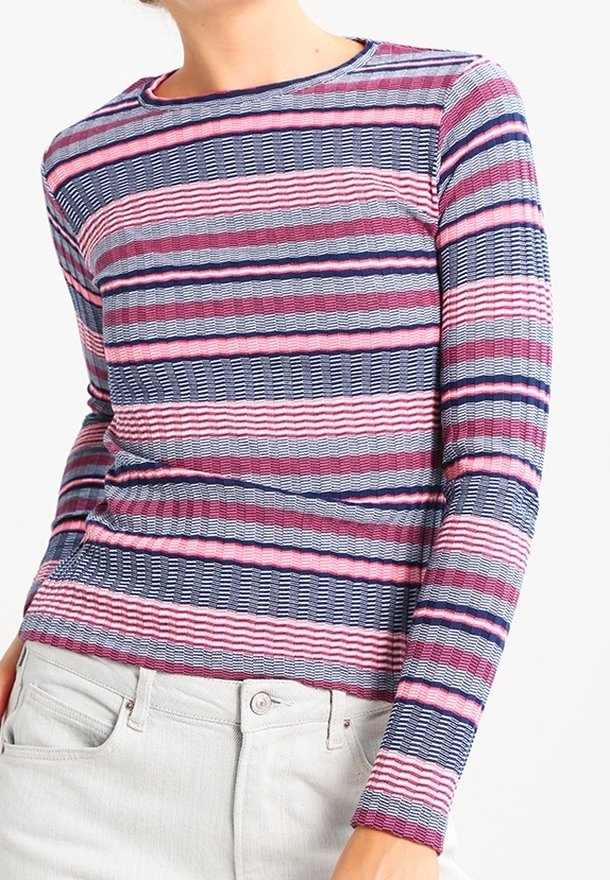 Haut ajusté à manches longues avec rayures horizontales en rose, violet, bleu marine et blanc, porté avec un pantalon de couleur claire.