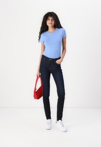 Camisa de manga corta azul claro, jeans ajustados azul oscuro, zapatillas blancas y un bolso rojo. Tejido suave, diseño ajustado, estilo casual.