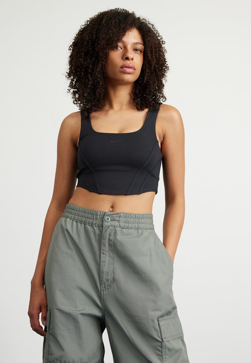 Top sportivo nero accorciato con scollo quadrato, caratterizzato da un logo del marchio discreto. Abbinato a pantaloni cargo larghi di un verde chiaro.