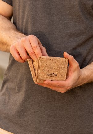 Cork wallet with a natural textured surface, folded design, and a zippered compartment. Features the brand name "Guist Leder" embossed on the front.