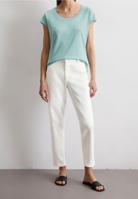 Ljusblå kortärmad t-shirt i kombination med vita raka byxor och svarta slidesandaler. Slät tygkvalitet och avslappnad passform.
