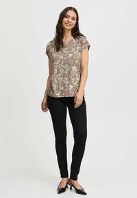 Brun blomstret bluse med korte ærmer, let stof, afslappet pasform, parret med sorte skinny bukser og sorte spidse højhælede sko.