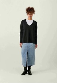 Mustavillasesta V-pääntiellä varustettu neule, valkoisen paidan päällä, yhdistettynä vaaleansinisestä denimistä valmistettuun maksihameeseen, jossa on edessä halkio, ja mustilla saappailla.