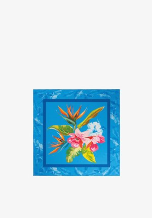 Kobieta poprawiająca niebieską kwiecistą chustę na głowie, ubrana w niebieską teksturowaną bluzkę, z długimi ciemnymi włosami i neutralnym makijażem, patrząca lekko na bok.