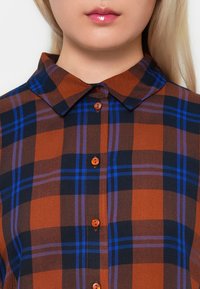 Plaid shirt with orange, blue, and black colors. Features a classic collar and button front, highlighting a textured fabric.