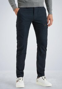 Tamno plave cargo hlače s višestrukim bočnim džepovima, slim fit dizajn i suptilan teksturiran površinski izgled, uparen s bijelim tenisicama.