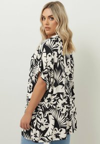 Svart och vit blommig skjorta med korta ärmar, lös passform, med djärva tropiska mönster, lättviktsmaterial och rund halsringning.