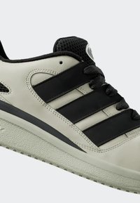 Sneaker in pelle grigia chiara con accenti neri, caratterizzato da tre strisce nere, suola in gomma testurizzata e linguetta in rete nera.