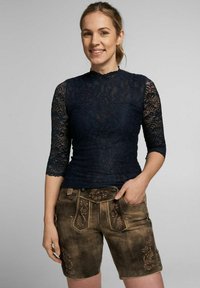 Marineblaues Spitzenoberteil mit Dreiviertelärmeln und Stehkragen, kombiniert mit braunen Leder-Shorts mit floralen Stickereien und Knopfdetails.