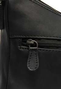 Angolo di una borsa in pelle nera con una cerniera, che mostra un materiale dalla texture liscia e una cerniera in metallo argentato con un linguetta in pelle.