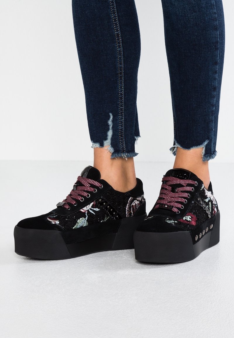 Svarta plattformssneakers i texturerat tyg, med blommig broderi, vinröda snören och nitar längs sidorna.
