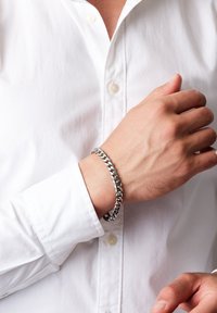 Silverkedja på en handled, med sammanslutna länkar, polerad yta och bärs med en vit skjorta.