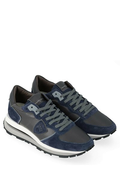 Un paio di sneaker blu navy e grigie con pannelli in suede e pelle, lacci grigi e suole bianche su sfondo bianco.