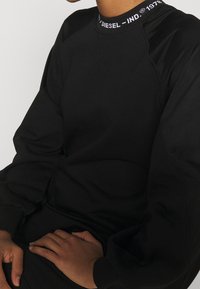 Svart sweatshirt i mjukt material, med ribbat krage med texten "DIESEL - IND" och raglanärmar för en avslappnad passform.