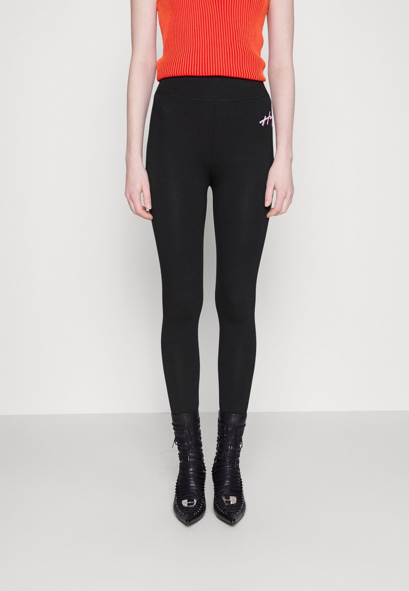 Leggings noirs au design ajusté, en matériau lisse, avec un petit détail de broderie rose. Associés à un haut rouge à côtes et des bottes noires.
