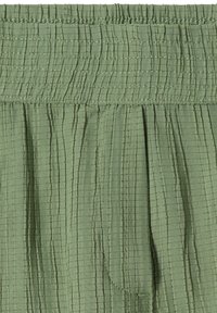 Tissu vert avec motif quadrillé cousu verticalement et horizontalement et bande élastiquée froncée sur le bord supérieur.
